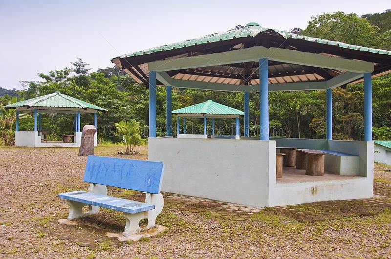 Three covered picnic areas and a blue bench by the side of the road.