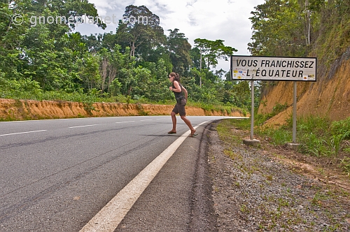 Western woman wearing shorts crosses the Equator on an open road.