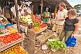Image of Two Western travellers buy vegetables at a market stall.
