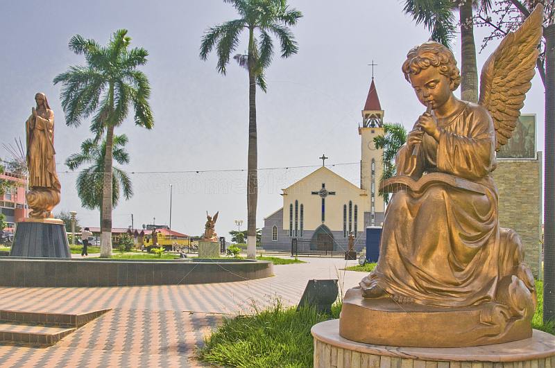 Golden statues of angel and Virgin Mary in front of the white and gray Roman Catholic church.