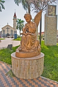 Golden statue of angel playing music in front of the white stucco Roman Catholic church.