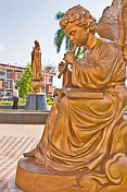 Golden statue of angel playing music in front man praying to the Holy Virgin Mary.