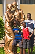 Three boys in football shirts stand in front of gold painted statue of dancing couple.