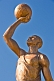 Image of Bronze painted statue of footballer holding a ball above his head.