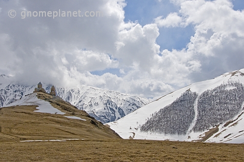 Snow-covered mountains contrast the bare stone of the Tsminda Sameba Monastery.