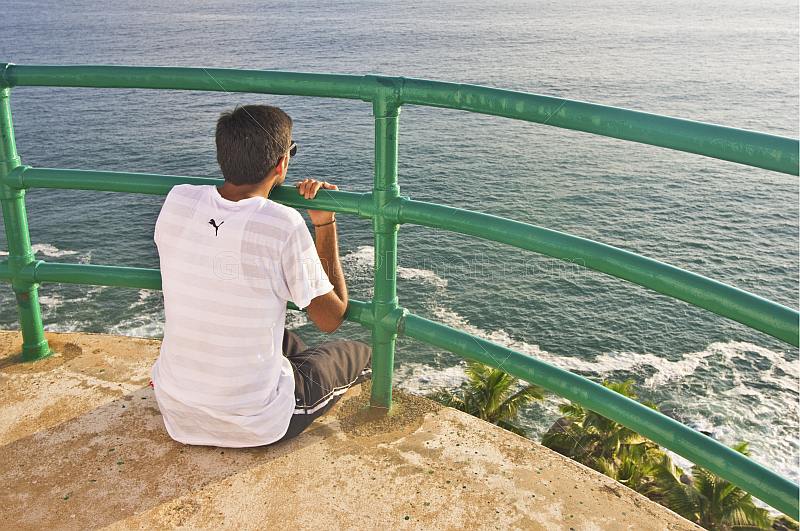 A young Indian male tourist looks out to sea from the observation gallery of Vizhinjam Lighthouse.