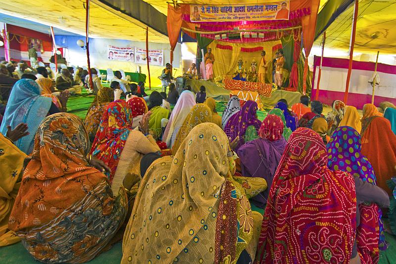 Village women dressed in saris sit on floor to watch Hindu religious play.