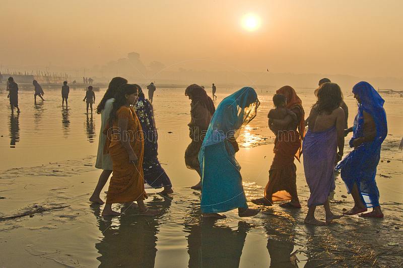 Women pilgrims in saris walk through muddy shallows to get to Ganges river bathing area.