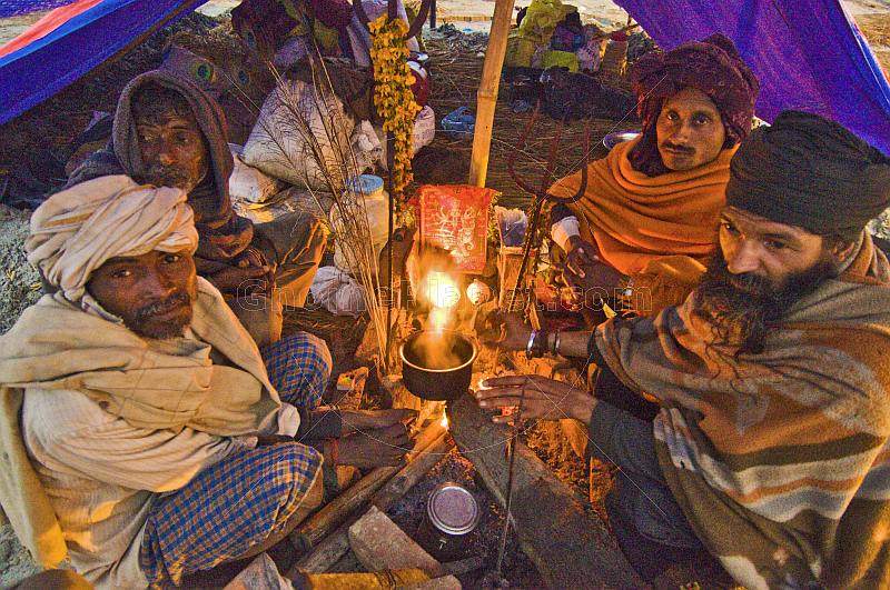 Four Hindu pilgrims huddle around campfire in tent whilst waiting for dawn at Kumbh Mela.