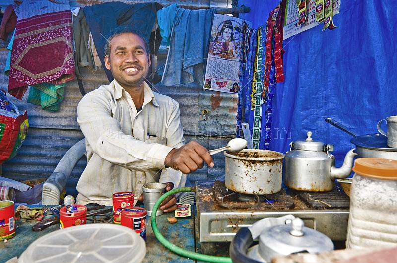 Smiling tea-stall owner adds sugar to pan of boiling Indian chai tea.