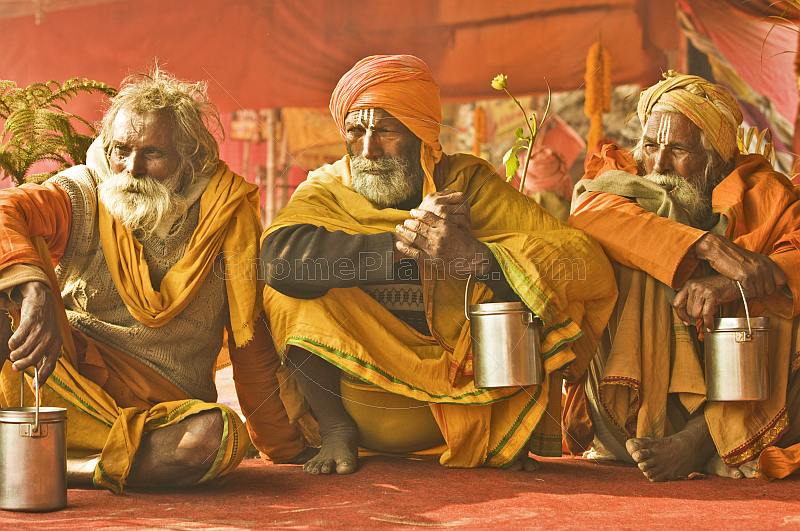Three saffron-clad Hindu Holy Men wait for alms in Juna Akhara festival tent.