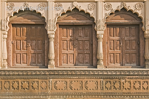 Three ancient brown wooden doors set in carved sandstone frames.