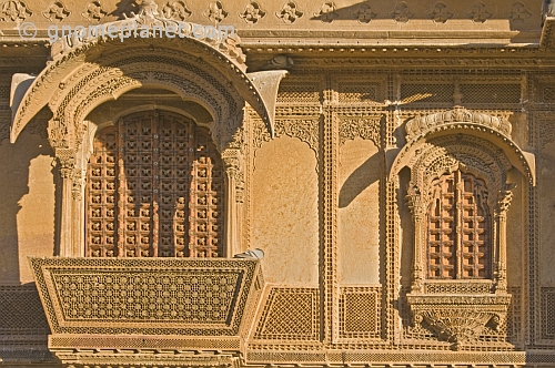 Richly-carved sandstone balcony with studded wooden doors on a havelli in the old quarter.
