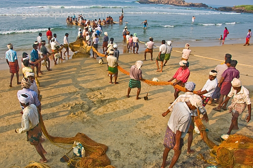 Fishermen struggle to haul their fishing net through the surf and on to the beach.
