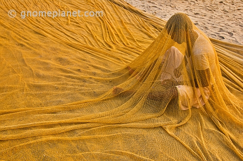 Fisherman sits inside his nets whilst reparing them.