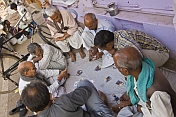 Old men play cards on a sheet spread on the sidewalk.