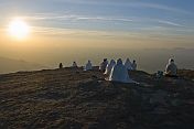 A group of Jain holy men meditate as the sun sets over the mountains.
