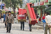 Porters carry a three-piece suite of furniture along the pedestrianised M.G. Marg.