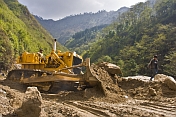 An Indian Army bulldozer deals with a sudden landslide that is blocking a mountain road.
