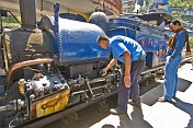 A passenger watches the engineer make adjustments to a steam locomotive on the Darjeeling Himalayan Railway.