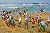 Fishermen struggle to haul their fishing net through the surf and on to the beach.