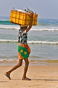 Man on the beach carrying a box of fish on his head.