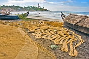 Fishermen dry their nets next to their boats on the beach.