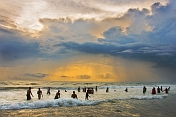 India, Kerala, Kovalam. Indian bathers play in the surf during a cloudy sunset.