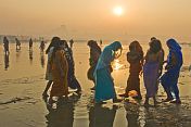 Women pilgrims in saris walk through muddy shallows to get to Ganges river bathing area.