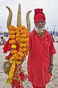 Hindu holy man dressed in red with marigold decorated brass trident for Lord Shiva.