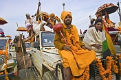 Saffron-clad temple staff ride on decorated jeeps for Basant Panchami Snana procession.