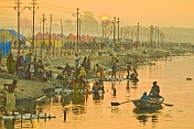 Solitary rowing boat passes bathing pilgrims on River Ganges in early dawn light.
