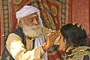 Elderly Holy Man in white turban applies sacred forehead mark to Hindu pilgrim woman.