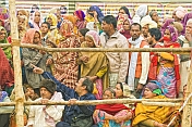 Villager pilgrims crowd behind barriers to see Basant Panchami Snana procession.