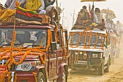 Decorated trucks drive through dust clouds in Basant Panchami Snana procession.