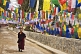 Image of Young trainee Buddhist monk walks past colorful prayer flags.