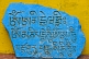 Buddhist religious text on a blue stone tablet resting against a yellow wall at the Pemayangtse Monastery.