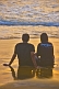 Indian couple with Pepe Jeans teeshirt watches sunset in the surf.
