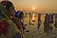 Image of Women pilgrims watch sunrise over ritual bathing area in Ganges Yamuna rivers.