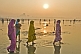 Image of Women pilgrims in saris walk through muddy shallows to get to Ganges river bathing area.