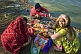 Two women and small boy prepare offerings for Hindu ceremony on Ganges River banks.