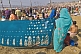 Woman dries blue Sari whilst watching bathing crowds in warm sunshine at Ganges Sangam.