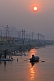 Image of Solitary rowing boat passes bathing pilgrims on River Ganges in early dawn light.