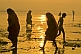 Women in saris walk through Ganges River shallows at dawn on way to ritual bath.