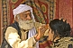 Image of Elderly Holy Man in white turban applies sacred forehead mark to Hindu pilgrim woman.