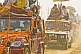 Image of Decorated trucks drive through dust clouds in Basant Panchami Snana procession.