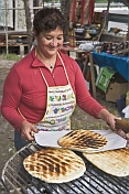 Woman cooks fresh bread over charcoal brazier.