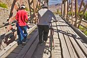 Two men with bicycle walk over a bridge near the Pucara Ruins.