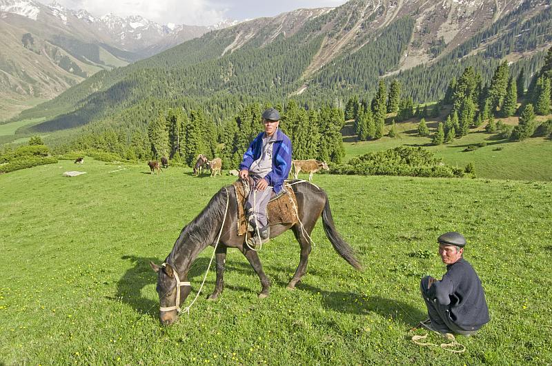 A Kyrgyz Horseman waits with his farmer friend as his horse crops the grass of the Altyn Arashan Mountains.