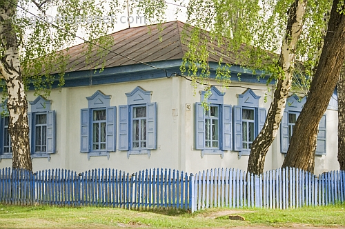 Russian-style painted cottage with picket fence, decorative windows and surrounding Birch trees.